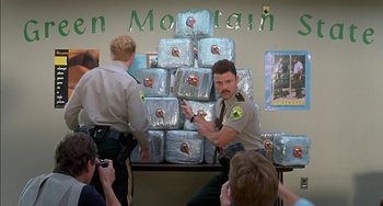 Movie still from “Super Troopers” (2001), directed by Jay Chandrasekhar – A man in a police uniform standing in front of stacks of ice; Medium shot, Low angle