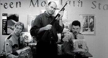 Movie still from “Super Troopers” (2001), directed by Jay Chandrasekhar – A man holding a rifle in front of another man holding a gun; Medium shot, Low angle