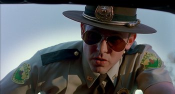 Movie still from “Super Troopers” (2001), directed by Jay Chandrasekhar – A man in a police uniform with sunglasses on; Close Up shot, Low angle
