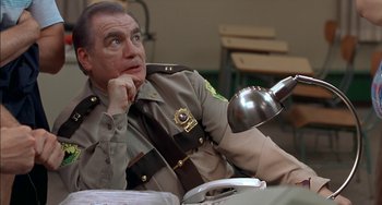 Movie still from “Super Troopers” (2001), directed by Jay Chandrasekhar – A police officer sitting at a table with his hand under his chin; Close Up shot, Low angle