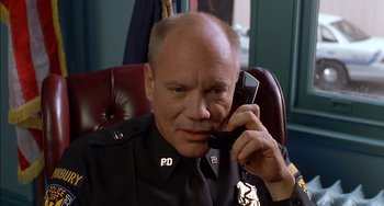 Movie still from “Super Troopers” (2001), directed by Jay Chandrasekhar – A police officer talking on a phone while sitting in a chair; Close Up shot, Low angle