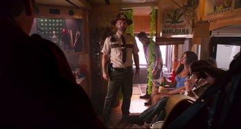 Movie still from “Super Troopers 2” (2018), directed by Jay Chandrasekhar – A group of people sitting in a room with a man in a uniform; Medium shot, Over the shoulder angle