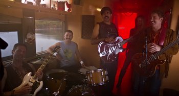 Movie still from “Super Troopers 2” (2018), directed by Jay Chandrasekhar – Two men are playing instruments in a room; Wide shot, High angle