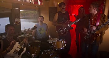 Movie still from “Super Troopers 2” (2018), directed by Jay Chandrasekhar – A group of men and a woman playing instruments; Wide shot, Low angle