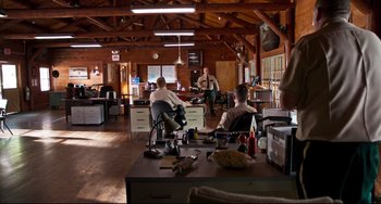 Movie still from “Super Troopers 2” (2018), directed by Jay Chandrasekhar – A group of people sitting at a table in a room; Wide shot, Over the shoulder angle