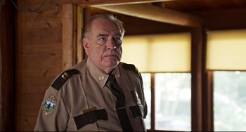 Movie still from “Super Troopers 2” (2018), directed by Jay Chandrasekhar – An older man wearing a uniform in front of a window; Close Up shot, Over the shoulder angle