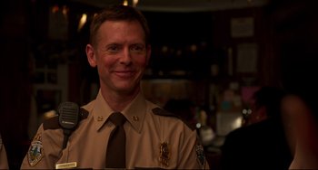 Movie still from “Super Troopers 2” (2018), directed by Jay Chandrasekhar – A man in a police uniform smiling for the camera; Close Up shot, Over the shoulder angle