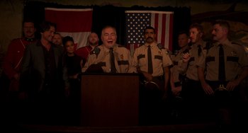 Movie still from “Super Troopers 2” (2018), directed by Jay Chandrasekhar – A group of men standing in front of a podium; Medium shot, Low angle