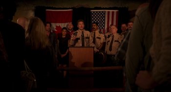 Movie still from “Super Troopers 2” (2018), directed by Jay Chandrasekhar – A group of people standing around a man in uniform; Wide shot, Over the shoulder angle