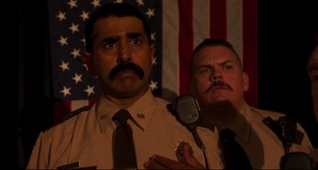 Movie still from “Super Troopers 2” (2018), directed by Jay Chandrasekhar – Two police officers in front of an american flag; Close Up shot, Over the shoulder angle