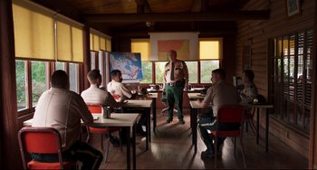 Movie still from “Super Troopers 2” (2018), directed by Jay Chandrasekhar – A group of people sitting at tables in a room; Wide shot, Over the shoulder angle