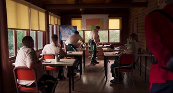 Movie still from “Super Troopers 2” (2018), directed by Jay Chandrasekhar – A group of people sitting at tables in a room; Wide shot, High angle