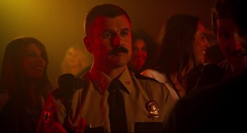 Movie still from “Super Troopers 2” (2018), directed by Jay Chandrasekhar – A man in a police uniform is holding a microphone in his hand; Close Up shot, Over the shoulder angle