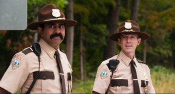 Movie still from “Super Troopers 2” (2018), directed by Jay Chandrasekhar – A couple of men standing next to each other in a forest; Medium shot, Over the shoulder angle