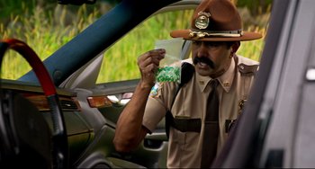 Movie still from “Super Troopers 2” (2018), directed by Jay Chandrasekhar – A police officer holding a bag of marijuana in his hand; Medium shot, Over the shoulder angle