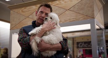 Movie still from “Super Troopers 2” (2018), directed by Jay Chandrasekhar – A man holding a white dog in his arms; Medium shot, Over the shoulder angle