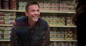 Movie still from “Super Troopers 2” (2018), directed by Jay Chandrasekhar – A man in a plaid vest is smiling in front of shelves of food; Medium shot, Over the shoulder angle