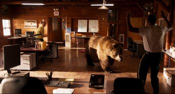 Movie still from “Super Troopers 2” (2018), directed by Jay Chandrasekhar – A large brown bear walking across a wooden floor; Extreme Wide shot, High angle