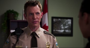 Movie still from “Super Troopers 2” (2018), directed by Jay Chandrasekhar – A man in a uniform standing in front of a canadian flag; Close Up shot, Over the shoulder angle