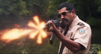 Movie still from “Super Troopers 2” (2018), directed by Jay Chandrasekhar – A police officer is holding a gun and aiming it with fire; Medium shot, Low angle