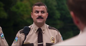 Movie still from “Super Troopers 2” (2018), directed by Jay Chandrasekhar – A man in a brown uniform is holding a microphone; Close Up shot, Low angle