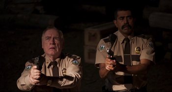 Movie still from “Super Troopers 2” (2018), directed by Jay Chandrasekhar – Two police officers are holding guns in their hands; Medium shot, Over the shoulder angle