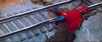 Movie still from “Superman II” (1980), directed by Richard Lester – A man dressed as superman climbing up a train track; Medium shot, Overhead angle