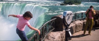 Movie still from “Superman II” (1980), directed by Richard Lester – A man standing next to a metal railing near a body of water; Extreme Wide shot, High angle