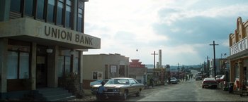 Movie still from “Superman II” (1980), directed by Richard Lester – An old car parked on the side of the street; Extreme Wide shot, High angle