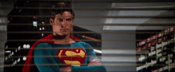 Movie still from “Superman II” (1980), directed by Richard Lester – A man in a superman costume standing in front of a window; Medium shot, Low angle
