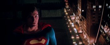 Movie still from “Superman II” (1980), directed by Richard Lester – A man dressed as superman standing in front of a street; Medium shot, Low angle