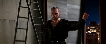 Movie still from “Superman II” (1980), directed by Richard Lester – A man in a black shirt is standing in front of a staircase; Medium shot, Low angle