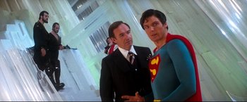 Movie still from “Superman II” (1980), directed by Richard Lester – A man in a suit standing next to a man in a superman costume; Medium shot, Low angle