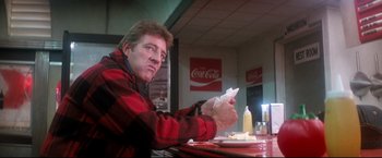 Movie still from “Superman II” (1980), directed by Richard Lester – A man sitting at a table in front of a coca - cola sign; Medium shot, Low angle