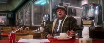 Movie still from “Superman II” (1980), directed by Richard Lester – A man sitting at a table with a cup of coffee; Medium shot, Low angle