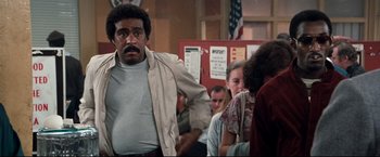 Movie still from “Superman III” (1983), directed by Richard Lester – A man standing in front of a group of people; Medium shot, Over the shoulder angle