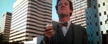 Movie still from “Superman III” (1983), directed by Richard Lester – A man in a suit and bow tie holding a doughnut; Close Up shot, Low angle