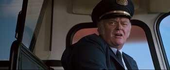 Movie still from “Superman III” (1983), directed by Richard Lester – A man wearing a uniform and a hat sitting in a chair; Close Up shot, Low angle