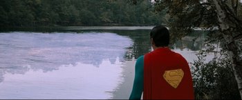 Movie still from “Superman III” (1983), directed by Richard Lester – A man wearing a superman cape standing on a lake shore; Wide shot, Over the shoulder angle