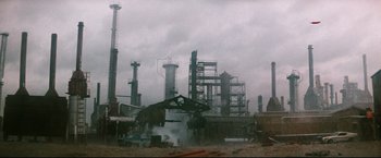 Movie still from “Superman III” (1983), directed by Richard Lester – An oil refinery is in the middle of a cloudy day; Extreme Wide shot, Low angle