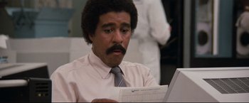 Movie still from “Superman III” (1983), directed by Richard Lester – A man in a white dress shirt and tie looking at a paper; Close Up shot, Low angle