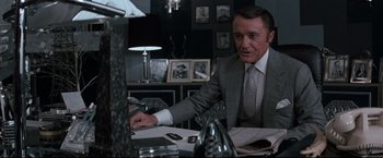 Movie still from “Superman III” (1983), directed by Richard Lester – A man sitting at a desk in a suit and tie; Medium shot, Over the shoulder angle