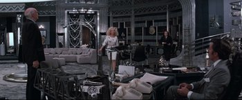 Movie still from “Superman III” (1983), directed by Richard Lester – A woman standing in front of a table in a living room; Wide shot, High angle