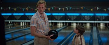 Movie still from “Superman III” (1983), directed by Richard Lester – A man holding a bowling ball while standing next to a child; Close Up shot, Low angle
