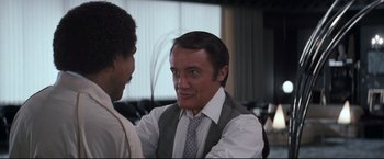Movie still from “Superman III” (1983), directed by Richard Lester – A man wearing a suit and tie talking to another man in a suit; Close Up shot, Over the shoulder angle
