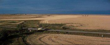 Movie still from “Superman III” (1983), directed by Richard Lester – A car driving down a dirt road near a field; Extreme Wide shot, High angle
