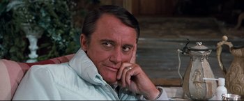 Movie still from “Superman III” (1983), directed by Richard Lester – A person sitting on a chair with his hand under his chin; Close Up shot, Over the shoulder angle