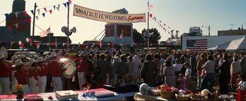 Movie still from “Superman III” (1983), directed by Richard Lester – A crowd of people standing under a banner; Extreme Wide shot, High angle