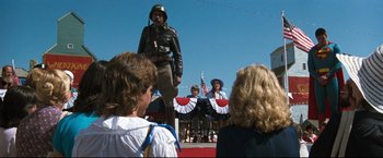 Movie still from “Superman III” (1983), directed by Richard Lester – A man in a uniform standing in front of a crowd of onlookers; Wide shot, Low angle