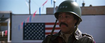 Movie still from “Superman III” (1983), directed by Richard Lester – A man in a military uniform with a flag in the background; Close Up shot, Low angle